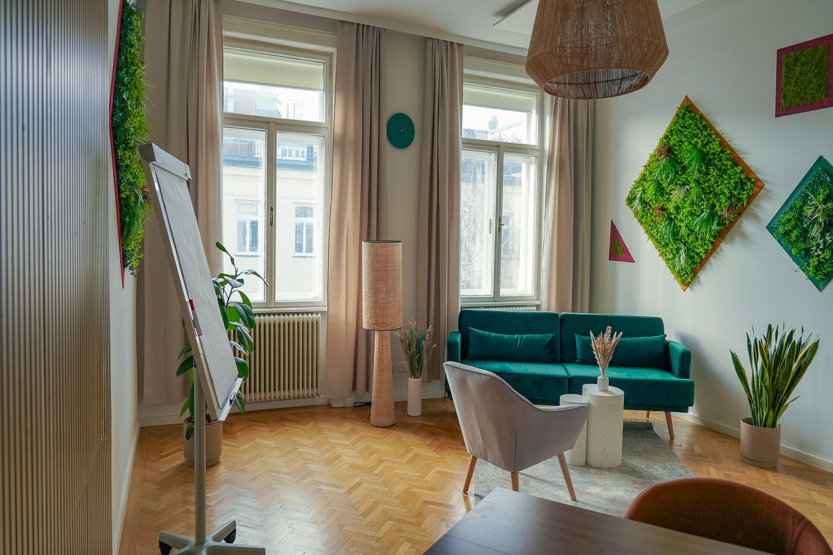 Praxisraum in 1030 Wien mit grünem Sofa, Flipchart und Pflanzenbildern
